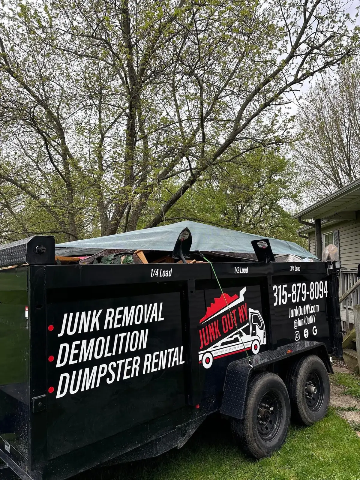 Junk Out NY roll-off dumpster trailer loaded and tarped at a residential job site
